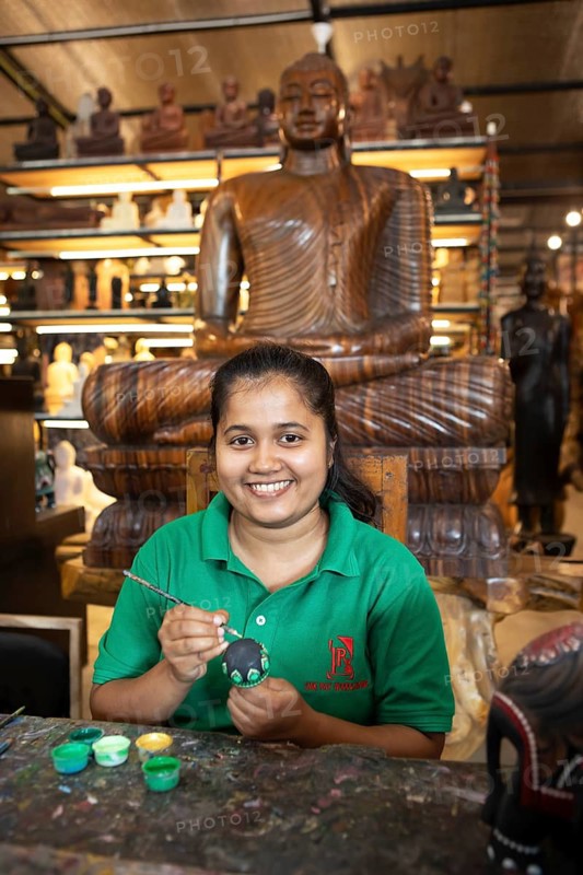Sri Lankan woman painting a wooden ball, behind a wooden Buddha, Oak Ray Woodcarvings, Naula, Matale, Central Province, Sri Lanka