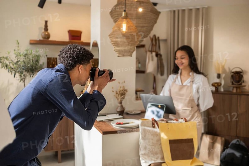 A photographer captures moments inside a stylish bag store, focusing on a staff member working behind a counter. The store is decorated with hanging lights and a variety of bags