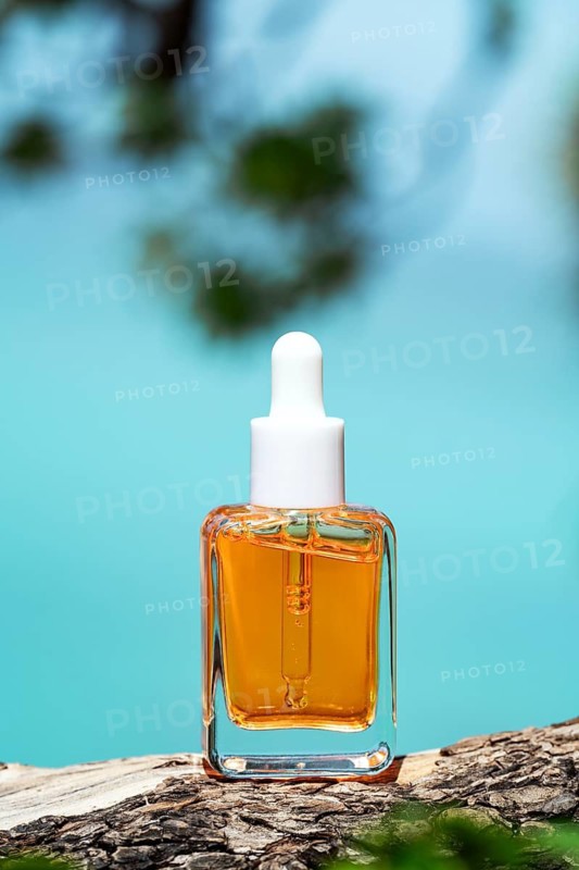 A luxurious cosmetic serum infused with vitamins, displayed on a rustic wooden log with the turquoise sea and blurred greenery in the background