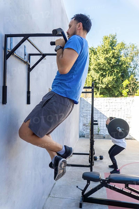 Determined male and female athletes performing pull-ups and squats in a functional training area, showcasing strength, fitness, and dedication to exercise