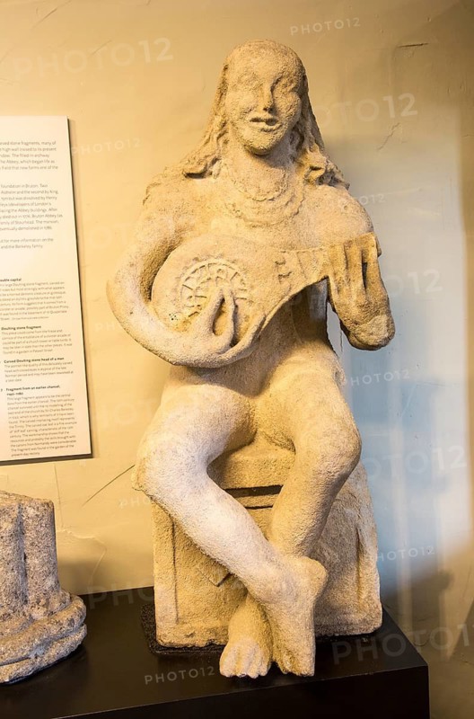 Female carved stone figure playing lute in museum at Bruton, Somerset, England, UK