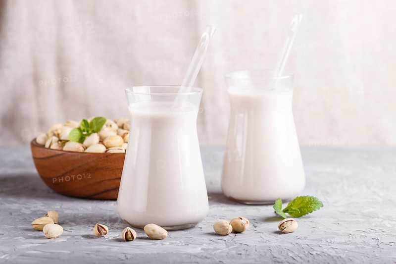 Organic non dairy pistachio milk in glass and wooden plate with pistachio nuts on a gray concrete background. Vegan healthy food concept, close up, side view