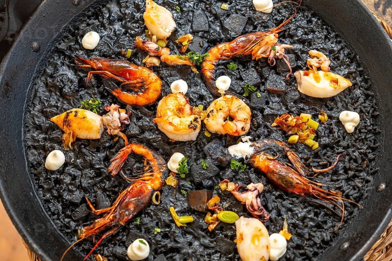 Close up of a black rice paella, featuring grilled prawns, squid, and aioli, showcasing the rich culinary heritage of mallorca