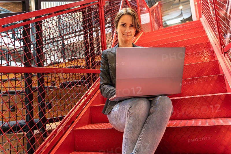 Confident businesswoman with laptop on red stairs looking at camera in modern office