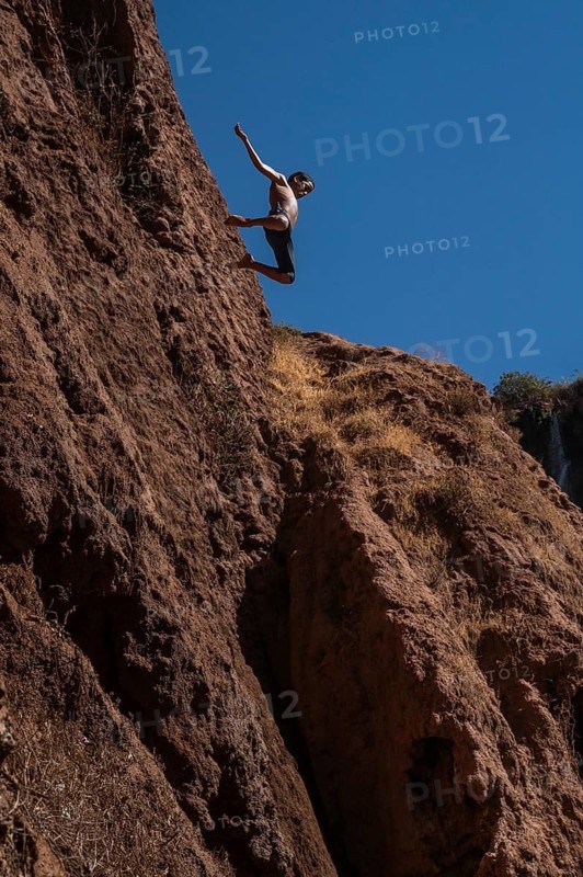 OUZOUD, MOROCCO - OCTOBER 5, 2024: A Moroccan young boy jumps from the high rock into the water under a waterfall Ouzoud
