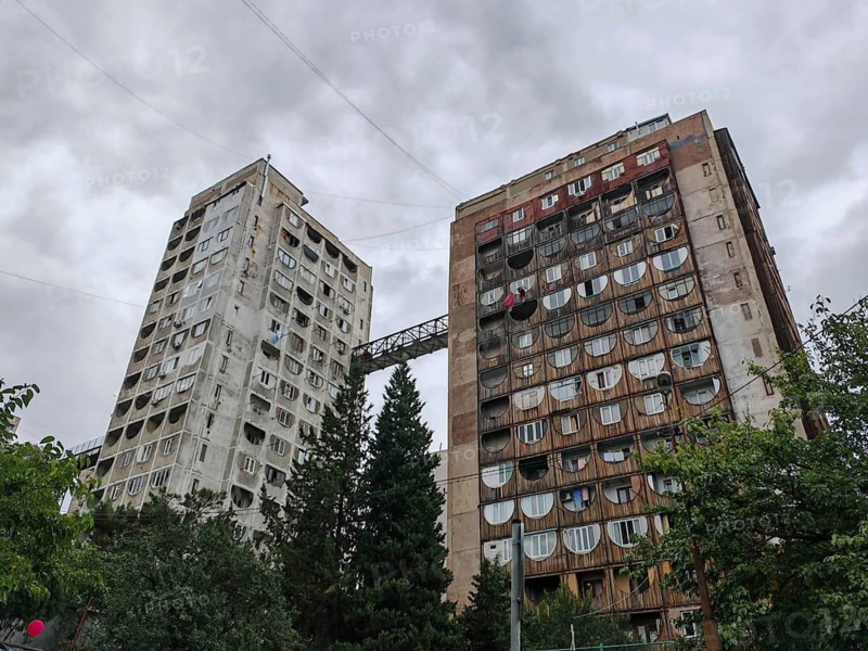 Two tall residential buildings with a bridge as a connection in a dramatic atmosphere in a wooded urban landscape, Tbilisi, Georgia