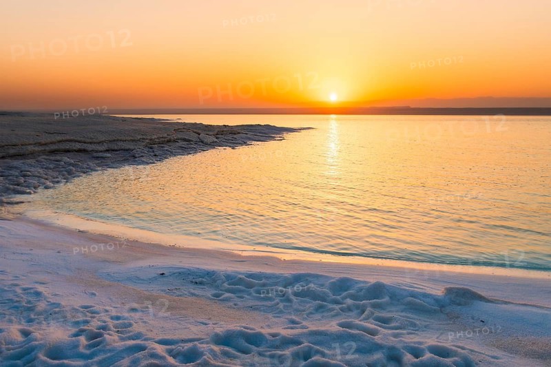 Dead Sea Jordan sunset with orange glow, calm water reflection, palm silhouettes, peaceful travel mood, nature beauty, climate and water scarcity concept