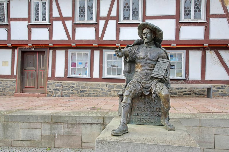 Philip the Magnanimous sculpture by Ewald Rumpf 2001, modern art, bronze sculpture, life-size, sitting man with historical clothing and Bible with inscription, The word of God would be eternal, Hessian church history during the Reformation, gesture, arms, index fingers, Philip I of Hesse, marketplace, Homberg-Efze, Hesse, Germany