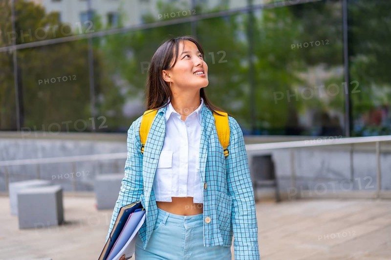 Happy asian student looking up with hopeful expression outside the university