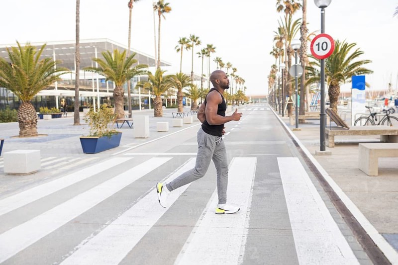 A cuban man jogs on a palm lined avenue, incorporating fitness into his lifestyle. The inviting urban setting features clear skies and modern architecture under palm trees