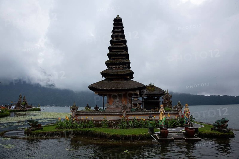 Traditional temple in Bali on a small island surrounded by calm water and clouds, Buddhist water temple Pura Ulun Danu Bratan with flowers, Bratan Lake, Bali, Indonesia