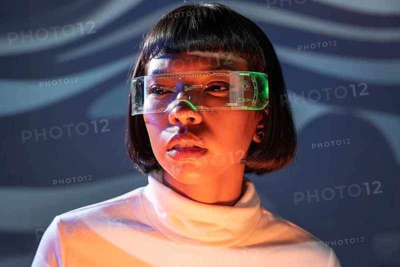 A Latin woman engages with futuristic virtual reality glasses in a modern setting. Her expression reflects focus and curiosity, highlighting the immersive nature of the experience