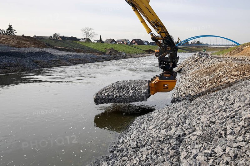 Dinslaken, Voerde, North Rhine-Westphalia, Germany - New Emscher estuary into the Rhine. Restoration of the dykes after dyke erosion during the 2023 flood. An excavator installs gabions and stone baskets on the riverbank. Renaturalisation of the Emscher. Flood protection by expanding the area. The mouth of the Emscher into the Rhine was moved almost 500 metres north from Dinslaken to Voerde. Fish can now swim barrier-free up the new Emscher from the Rhine through a newly created floodplain area. Following the construction of a parallel sewer, the Emscher has been completely free of sewage since January 2022. The river was previously an open, above-ground combined sewer with rainwater and wastewater