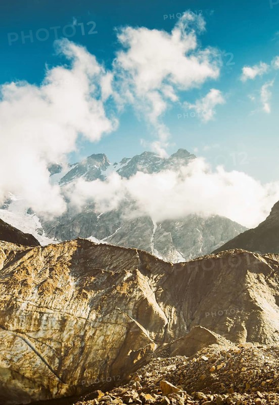 Georgia Svaneti Shkhara glacier summer morning with clouds drift across rugged peaks, moraine rocks foreground .Smoky mountains concept