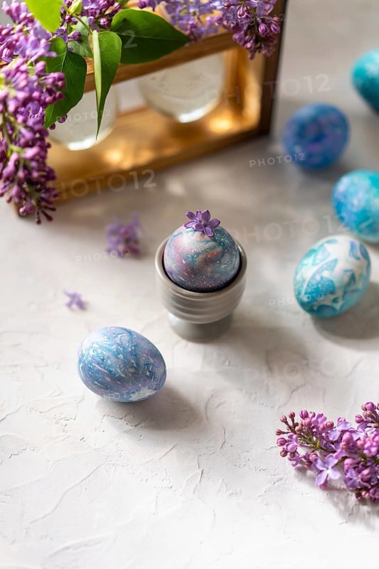 Vibrant, hand painted Easter eggs with marbled patterns surrounded by fresh lilac flowers, set on a textured surface. Perfect for a spring or Easter theme
