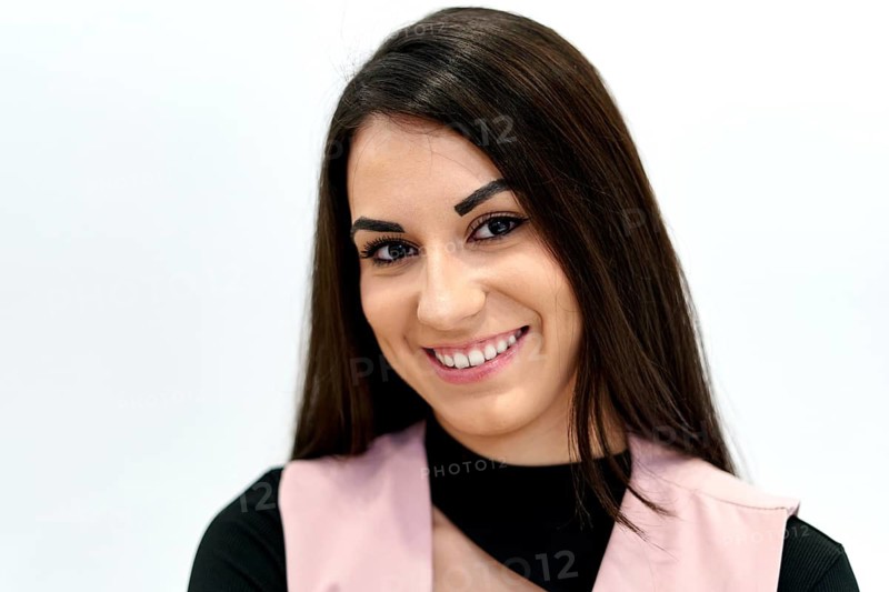 Cheerful woman in a dental clinic setting, wearing a pink uniform and smiling warmly. Her expression conveys a welcoming and professional atmosphere for patients