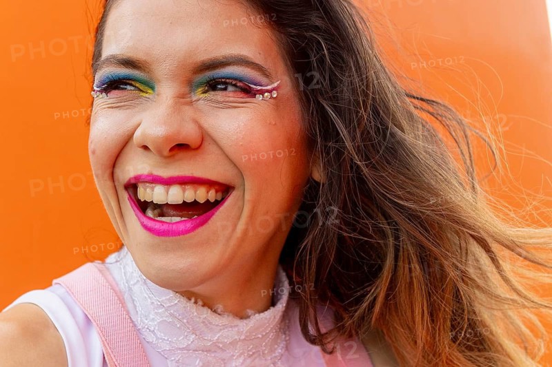 Celebrate diversity and artistry with this vibrant image of a woman radiating joy. Showcasing colorful, creative makeup, this image embodies LGBTQIA+ pride and self-expression
