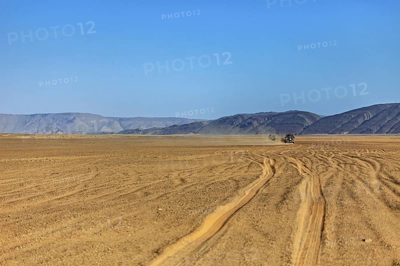 Jeep drives through dusty, barren desert with mountain formations, Off-road vehicle through the endless landscape of the Sahara desert in Algeria