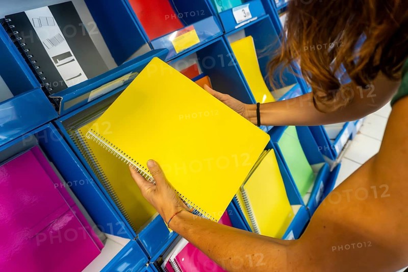 A woman is holding a yellow spiral notebook in a store. The notebook is on a shelf among other notebooks. Back to school concept