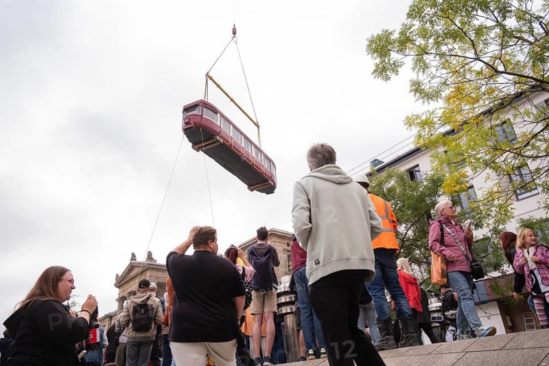 Many on the station forecourt as an old suspension railway wagon is lifted with a truck-mounted crane into an intermediate building of Wuppertal Central Station, Wuppertal, Germany
