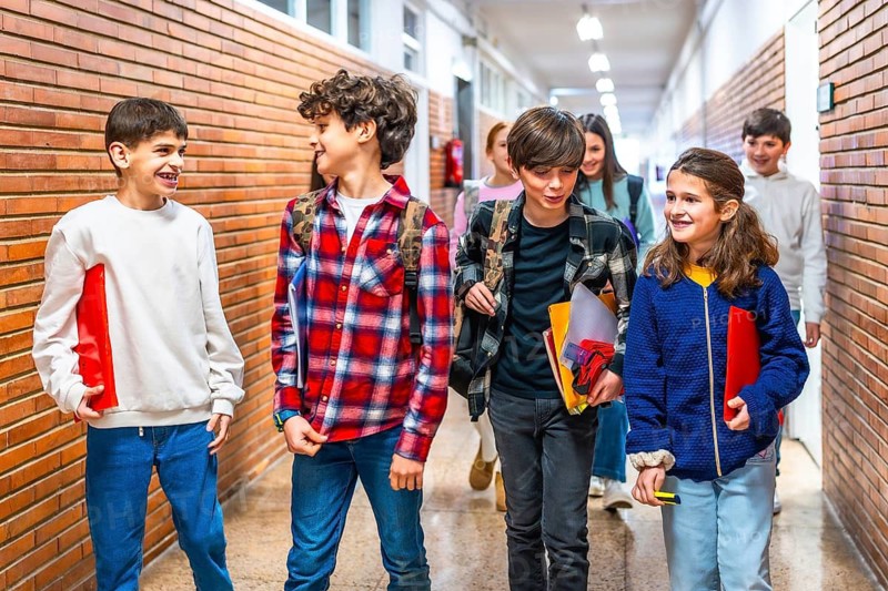Cheerful students carrying folders and backpacks are walking together down school hallway after class