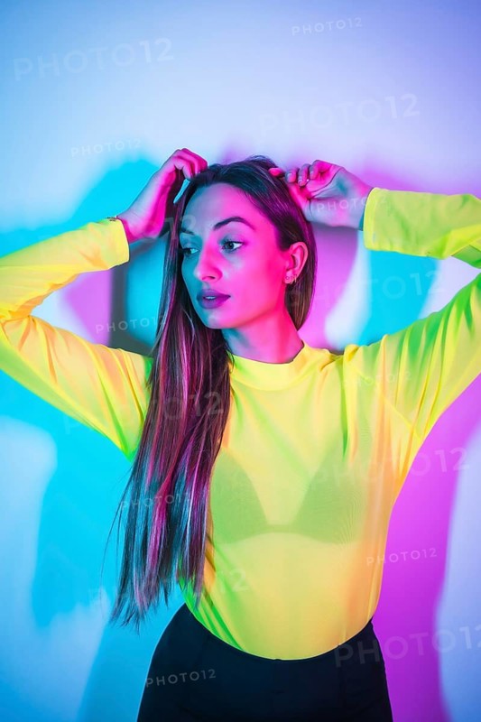 Party lifestyle in a nightclub with pink blue neon lights, portrait of a young blonde caucasian girl in a yellow t-shirt
