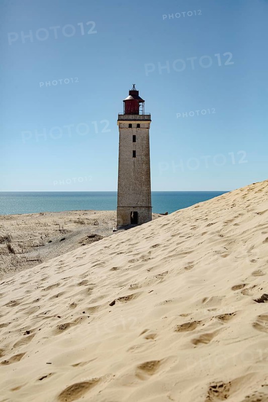 A lighthouse on the coast, surrounded by dunes, with the sea on the horizon, lighthouse in the Rubjerg Knude hiking dune, Jutland, Denmark