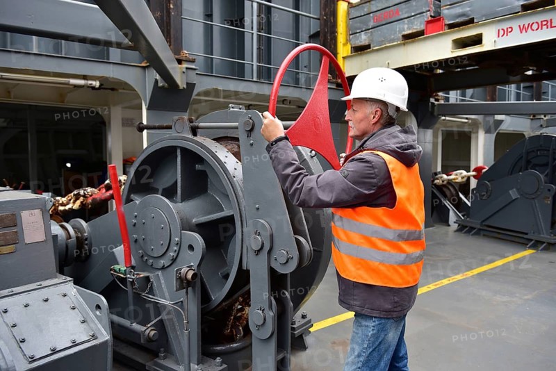 A worker wearing helmet and vest operates a large machine on a ship in an industrial environment, worker with the anchor chain on a container ship, Schleswig-Holstein, Germany