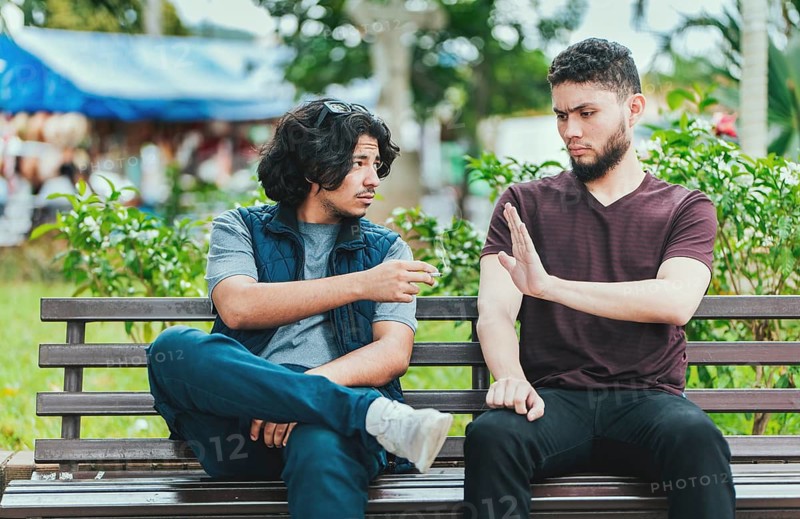 Disgusted guy sitting refusing a cigarette. Young man sitting refusing a cigarette in the park