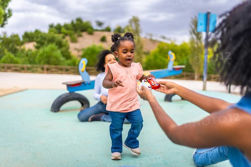 Baby african girl walking to her mother to pick a toy in a public park