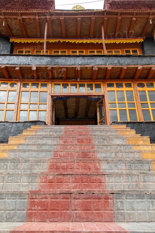 Steps lead to a traditional building in the scenic Zanskar Valley, Ladakh, India. The architectural design showcases vibrant colors and wooden elements, typical of the region