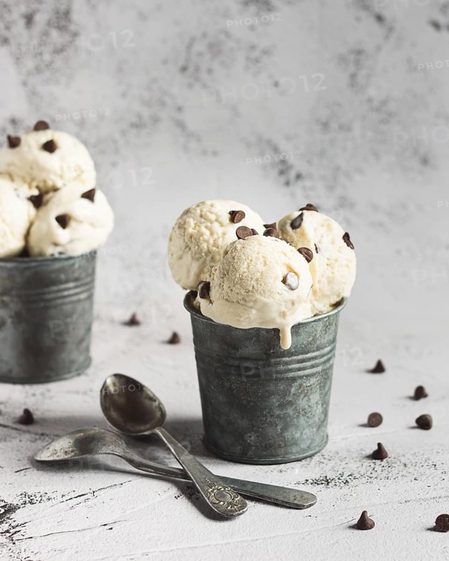 A refreshing treat of banana ice cream made with creamy Greek yogurt, ripe bananas, and rich chocolate chips. Perfectly chilled and served in a rustic metal cup with scattered chocolate chips