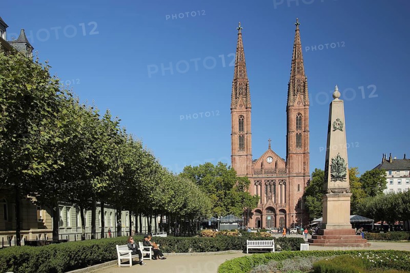 Waterloo obelisk and twin towers of the neo-gothic St. Boniface church, war memorial, park benches, Luisenplatz, Wiesbaden, Taunus, Hesse, Germany