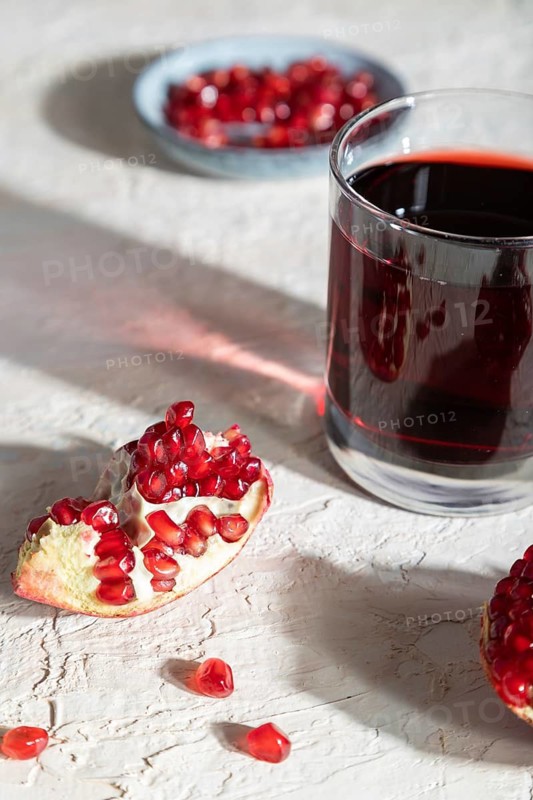 Glass of pomegranate juice on a white concrete background. Hard light, contrast. Side view, close up, selective focus