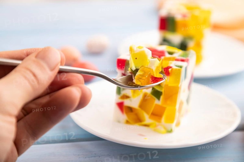 Colored Fruit and milk jelly with hand on blue wooden background and orange linen textile, side view, close up, selective focus