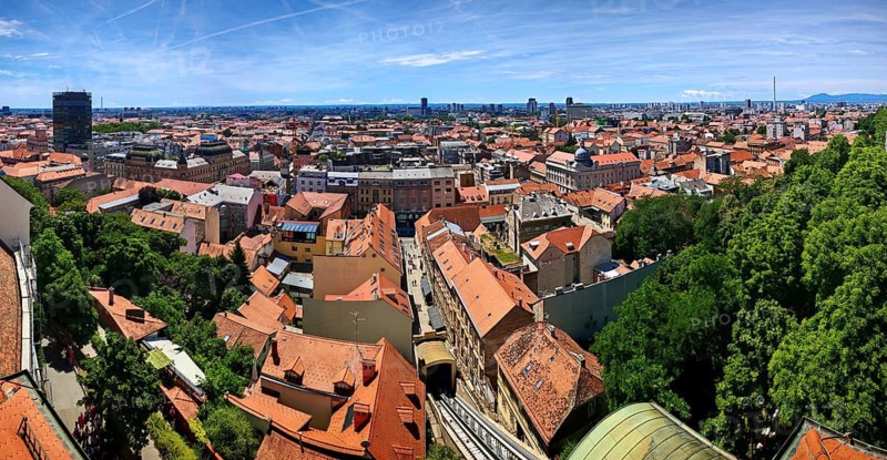 Panoramic view from Lotrscak Tower over a city with tiled roofs and an urban skyline surrounded by trees, Zagreb, Croatia