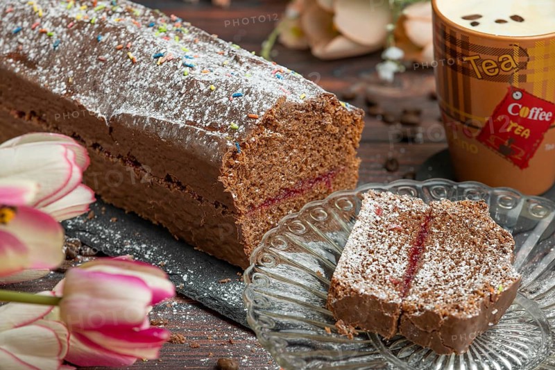 Chocolate cake dusted with icing sugar next to coffee on a wooden table with flowers