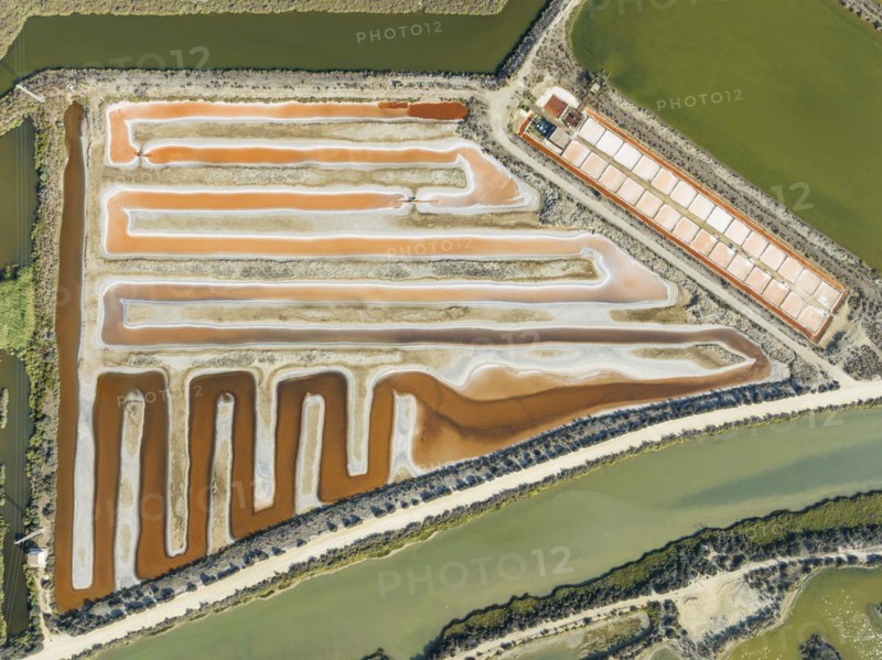 Saline ponds at the salt works near Chiclana de la Frontera. The orange-red colour depends on the level of salinity and is directly caused by the algae Dunaliella salina and brine shrimp. Aerial view. Drone shot. Cádiz province, Andalusia, Spain