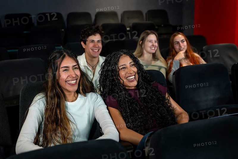 Friends laughing and enjoying a comedy movie at the cinema, sharing joyful moments together in a relaxed and fun atmosphere