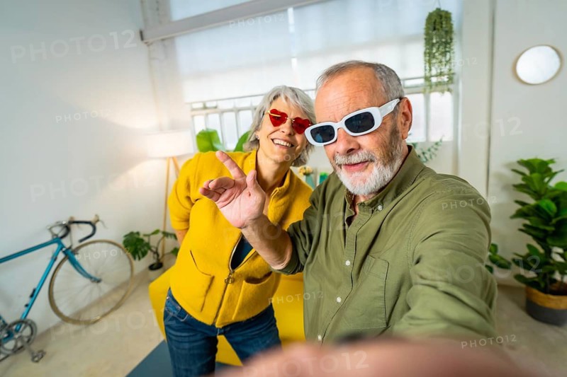 Modern senior couple taking a selfie while having fun together wearing fun sunglasses and dancing at home