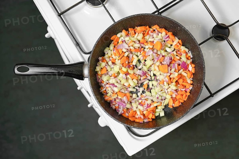 Top view of chopped carrots, onions, and celery in a skillet on a home kitchen stove, creating a flavorful base for various dishes