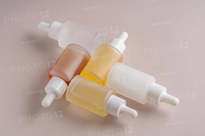 A top view of assorted dropper bottles with varying translucent hues, neatly arranged on a smooth beige surface, reflecting a clean and minimalist aesthetic