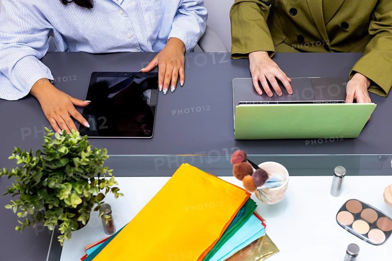 Two professionals collaborate using technology devices, surrounded by fabric swatches and makeup, during an image consulting session focused on color and style enhancement