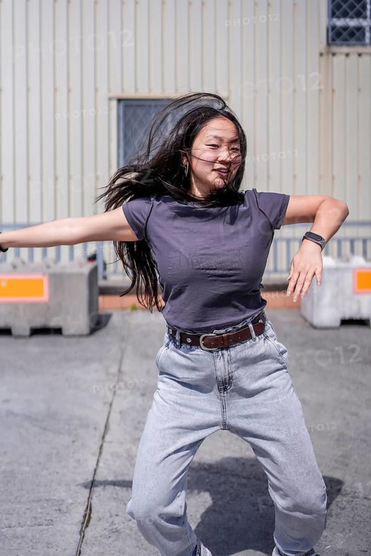 Vertical photo of a beauty female asian dancer moving arms in a futuristic robotic way dancing outdoors in an industrial urban space