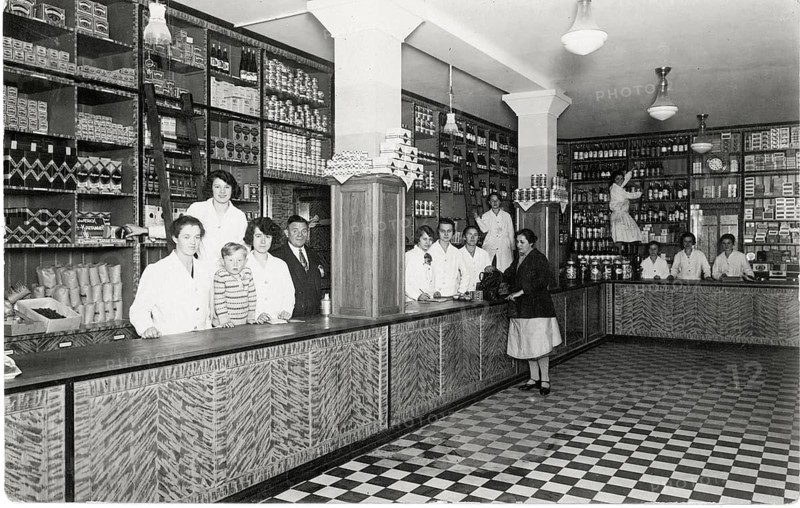 Colonial goods, shop counter, exclusive shop, sale, shop, profession, twenties, saleswoman, a long shop counter with several people behind it, surrounded by full shelves, around 1924