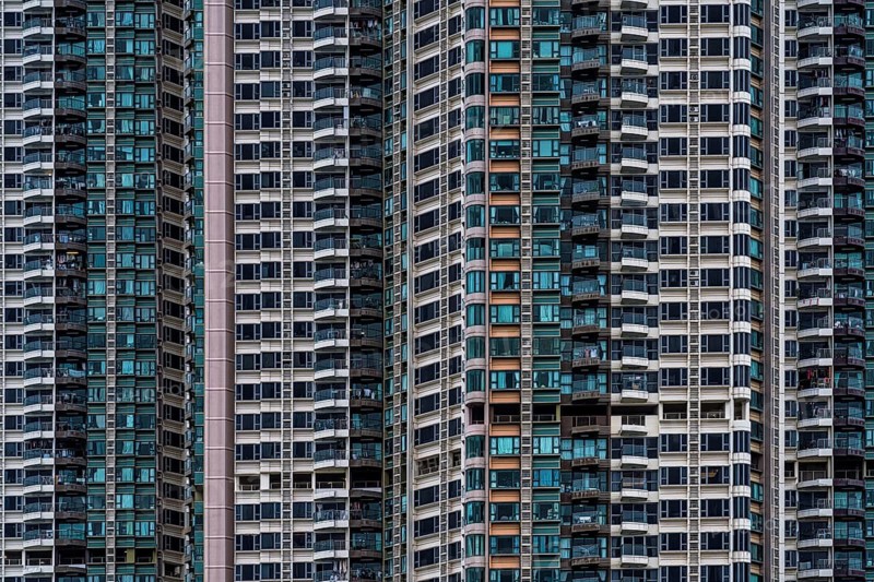 A striking architectural photography capturing the dense and detailed facade of modern high-rise residential buildings in Hong Kong, showcasing a variety of window patterns and balcony designs