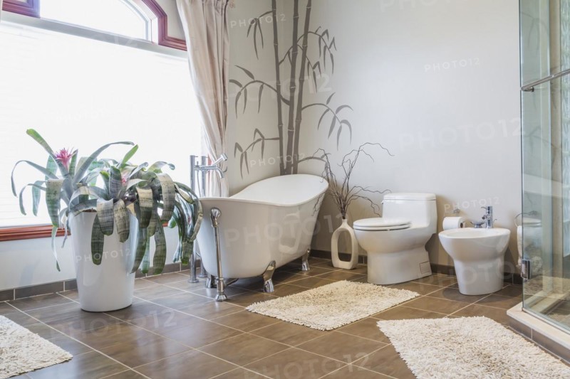 Freestanding bathtub, bidet, clear glass shower stall in en suite with grey nuanced ceramic tile floor on upstairs floor inside a luxurious residential home, Quebec, Canada