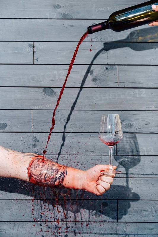 A visually striking composition of red wine being poured into a glass through a tattooed arm, creating a surreal and artistic effect. A bold and unconventional concept for restaurant branding and marketing