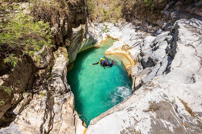 A canyoneer is captured in mid-flight in a dynamic jump into a shimmering turquoise pool surrounded by smooth canyon walls in Matacanes, Nuevo Leon, Mexico. Pure adrenaline and freedom