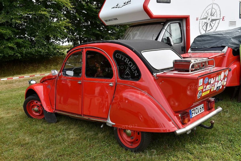 A red Citroën 2CV is parked next to a motorhome with lots of stickers, vintage Citroën 2CV6 at a duck meeting in Kropp, Schleswig-Holstein, Germany